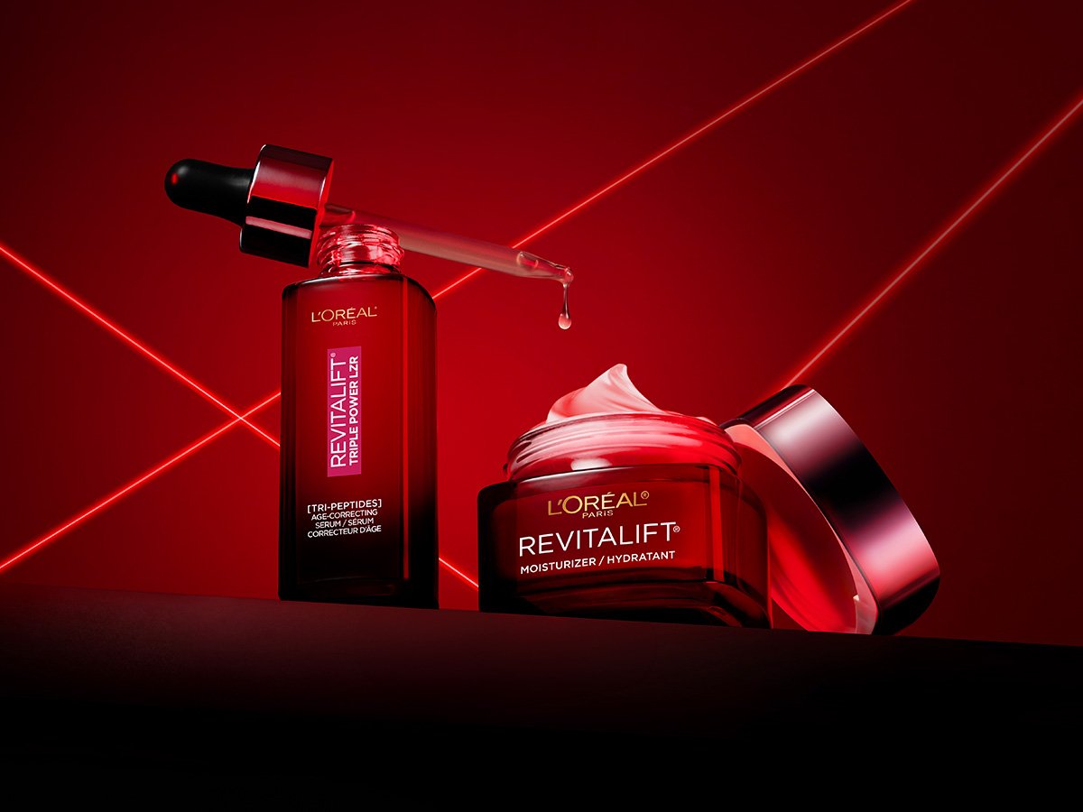 L'Oréal Revitalift Triple Power LZR products: a dropper serum and an open moisturizer jar, staged with red laser lines against a dark red background.